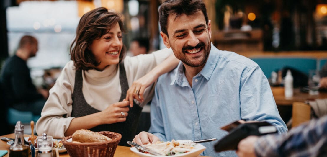 Ein Paar bezahlt kontaktlos mit einer Kreditkarte an einem Tisch in einem Restaurant.