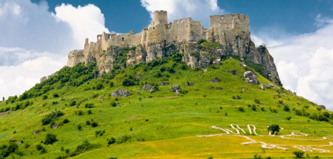 Eine Burganlage auf einem Berg, umringt von grünen Wiesen