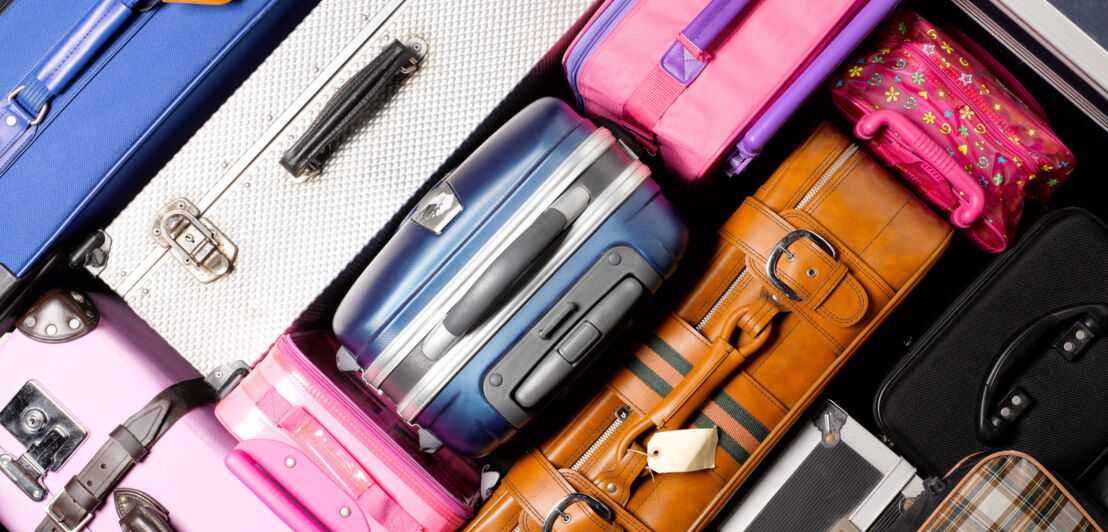 Aufsicht mehrerer Koffer in unterschiedlichen Farben und Materialien. 