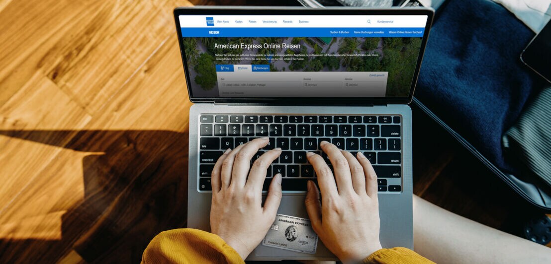 Aufsicht zweier Hände an einem Laptop bei der Buchung einer Reise über den American Express Online-Reiseservice mit einer Platinum Card