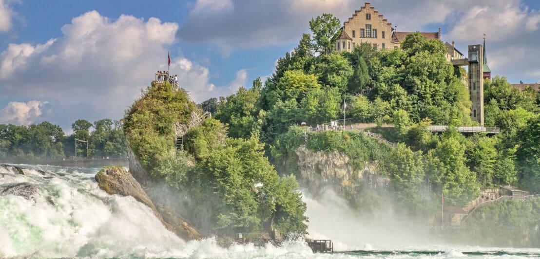 Ein Schloss auf einem dichtbewachsenen Felsen oberhalb eines Wasserfalls