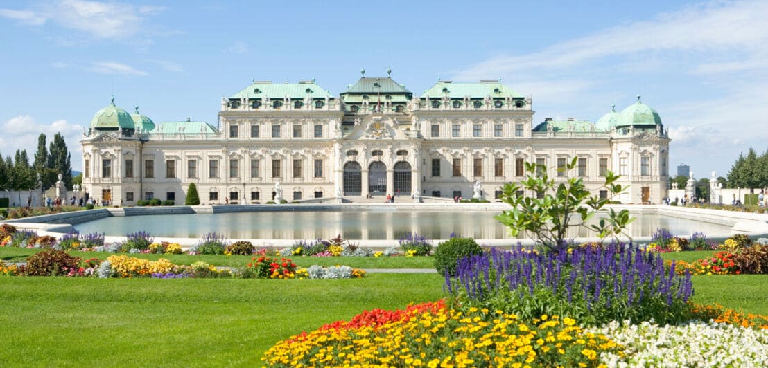 Barockschloss Belvedere mit Teich und Parkanlage mit blühenden Pflanzen im Vordergrund