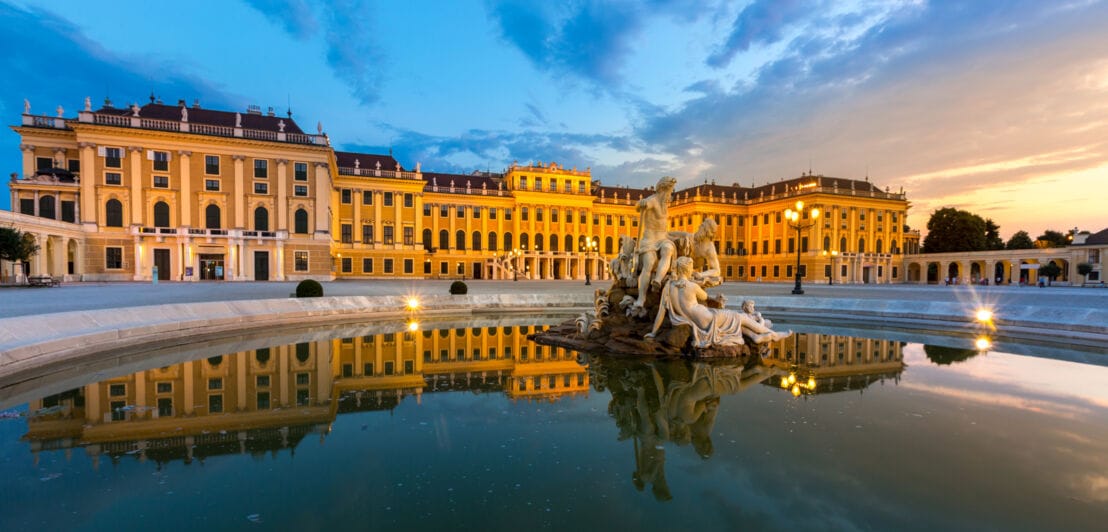 Beleuchtetes Schloss Schönbrunn mit Brunnen im Vordergrund bei Nacht