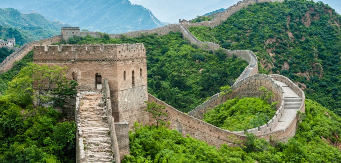 Abschnitt der Chinesischen Mauer mit Wachtürmen in einer bewaldeten Hügellandschaft
