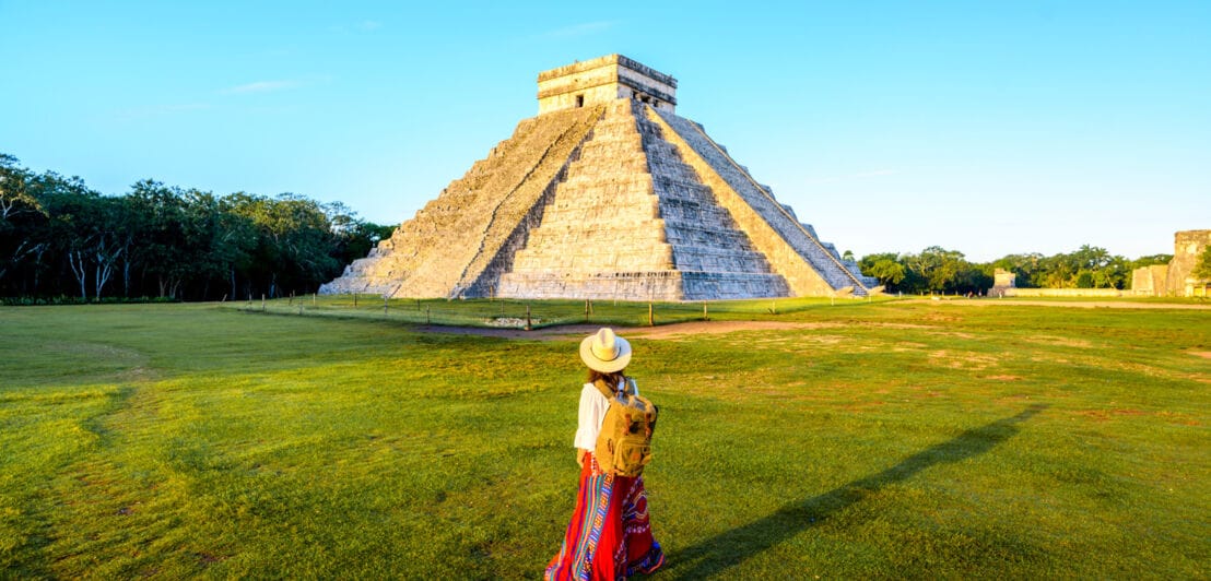 Rückansicht einer Frau mit Strohhut vor einer Stufenpyramide