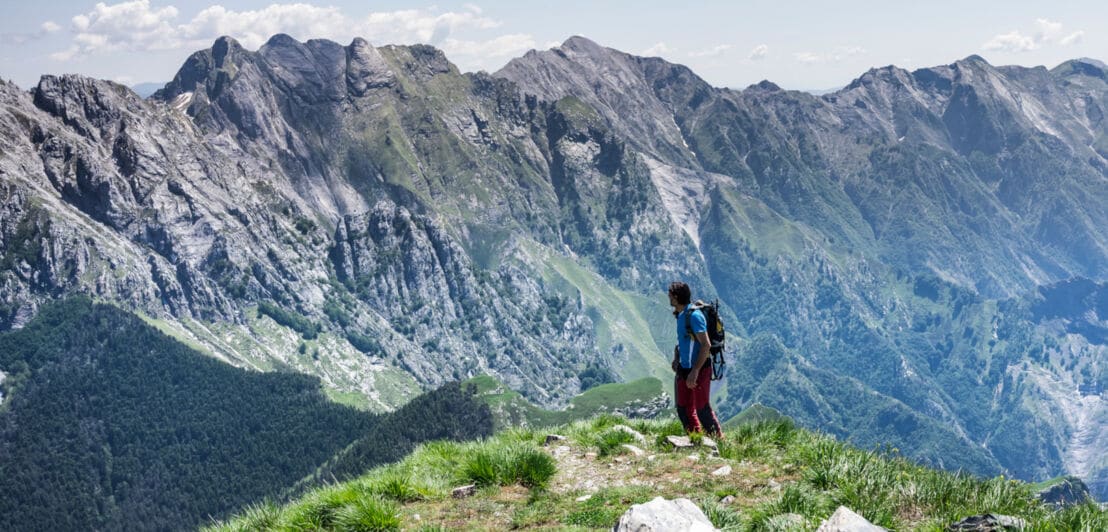 Eine Person steht auf einem Bergkamm, im Hintergrund ist eine Bergkette zu sehen