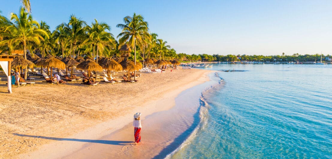 Eine Frau geht einen karibischen, palmengesäumten Sandstrand entlang