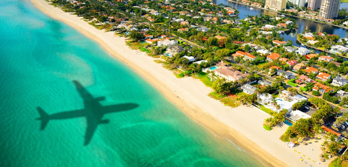 Luftaufnahme von Miami Beach mit dem Schatten eines Flugzeuges im türkisblauen Meer.