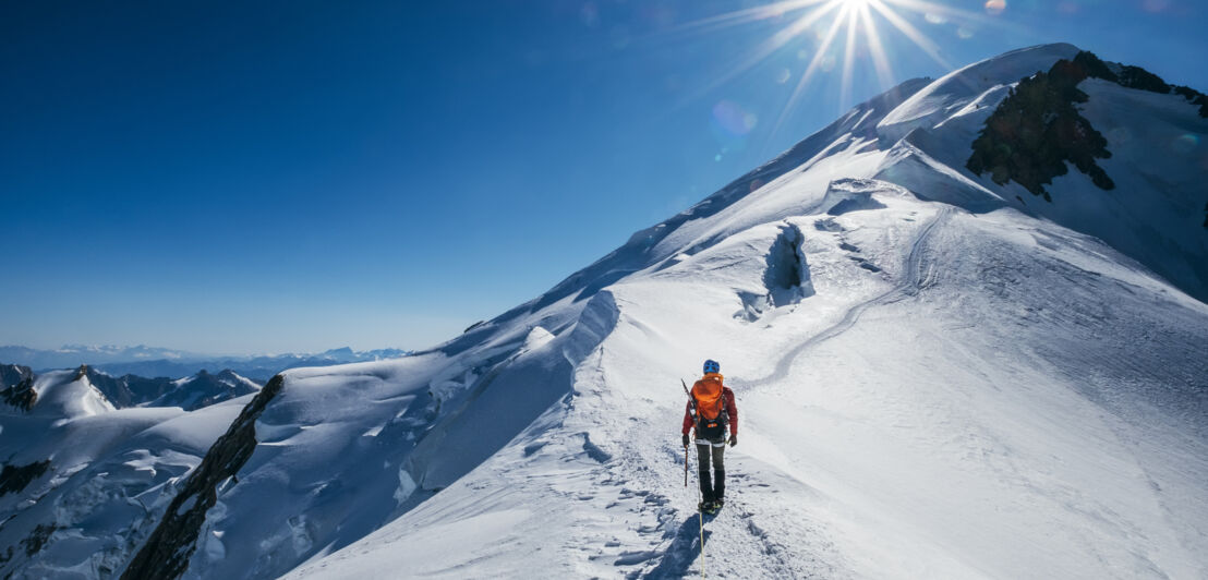 Eine Person läuft einen verschneiten Bergkamm in Richtung des Gipfels hinauf