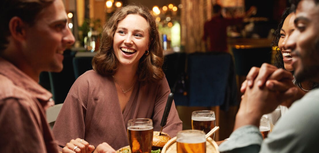 Zwei Frauen und zwei Männer sitzen an einem Tisch bei Burgern und Bier