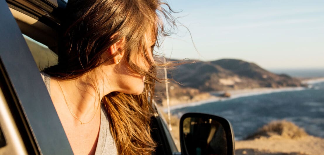 Profil einer Frau, die aus einem Autofenster auf ein Küstenpanorama schaut