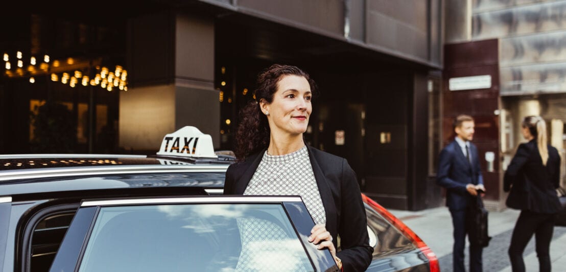 Eine Frau steigt aus einem schwarzen Taxi vor einem Hotel.