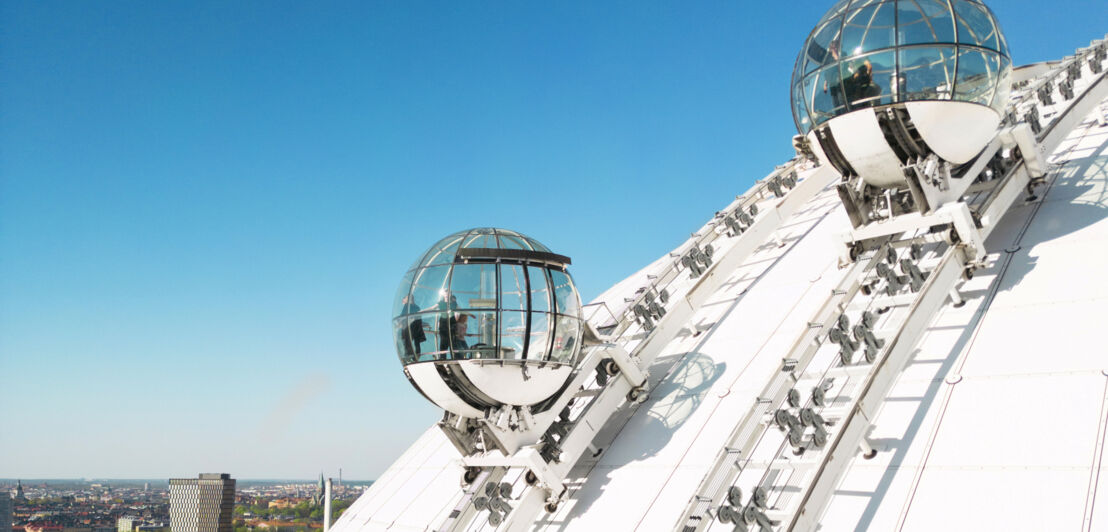 Zwei Aufzüge mit Glasgondeln auf einem Dach mit Blick auf Stockholm.