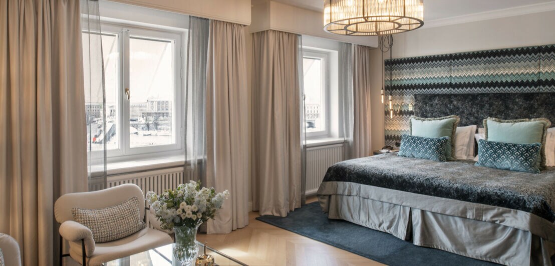 Luxuriöses, helles Hotelzimmer mit Kingsize-Bett und Textilien in Blau- und Beigetönen.