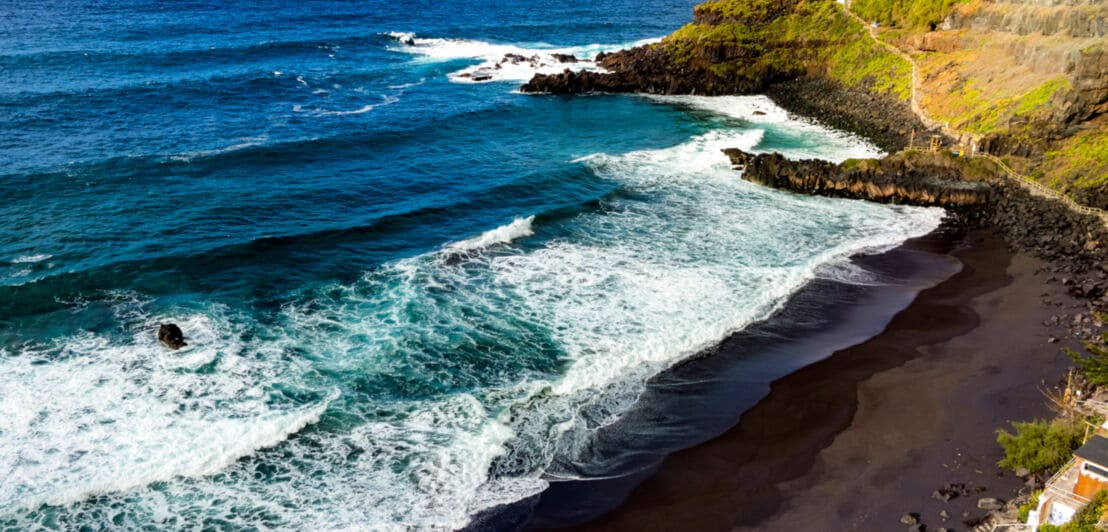 Aufsicht einer menschenleeren Strandbucht mit schwarzem Vulkansand