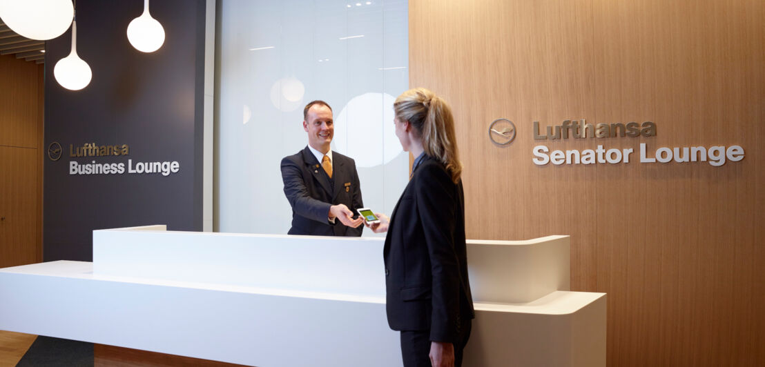 Eine Frau checkt bei einem Mitarbeiter an der Rezeption einer Lufthansa Lounge ein.