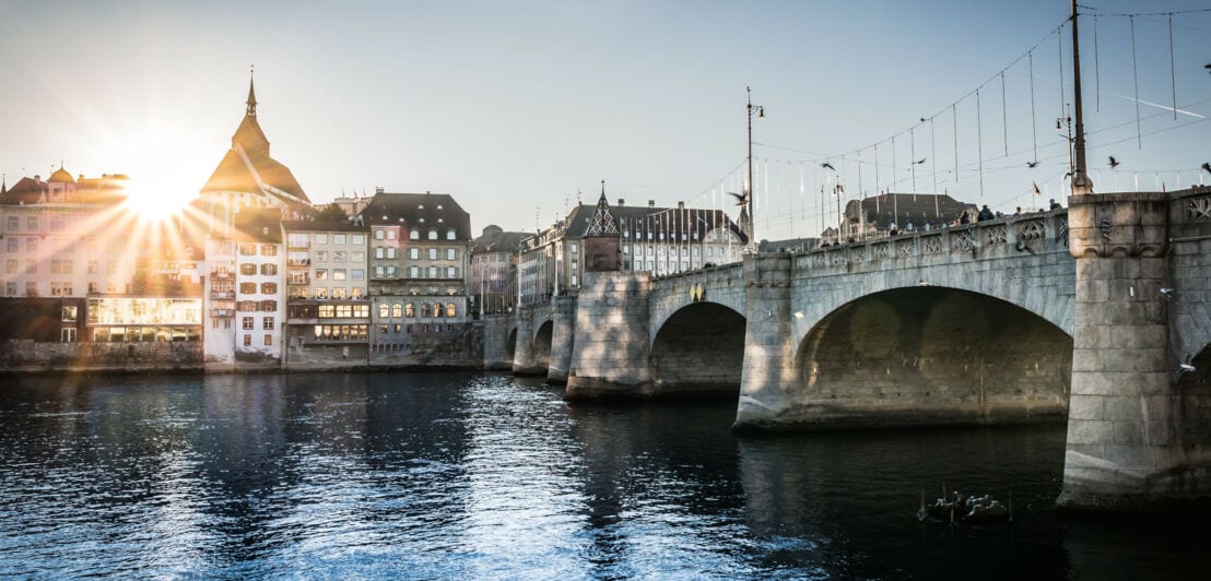 Eine große Steinbrücke über dem Rhein, im Hintergrund mehrere Gebäude in der Abendsonne.