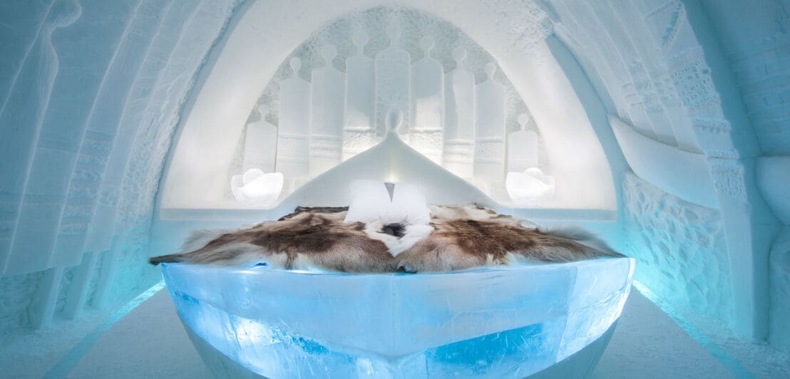 Innenansicht eines Zimmers in einem Eishotel mit Rentierfellen auf dem Bett.