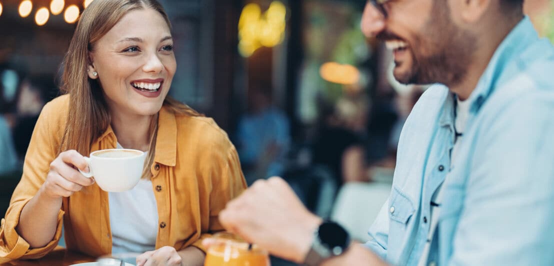 Ein lachendes Paar beim Kaffee trinken an einem Tisch in einem Restaurant.