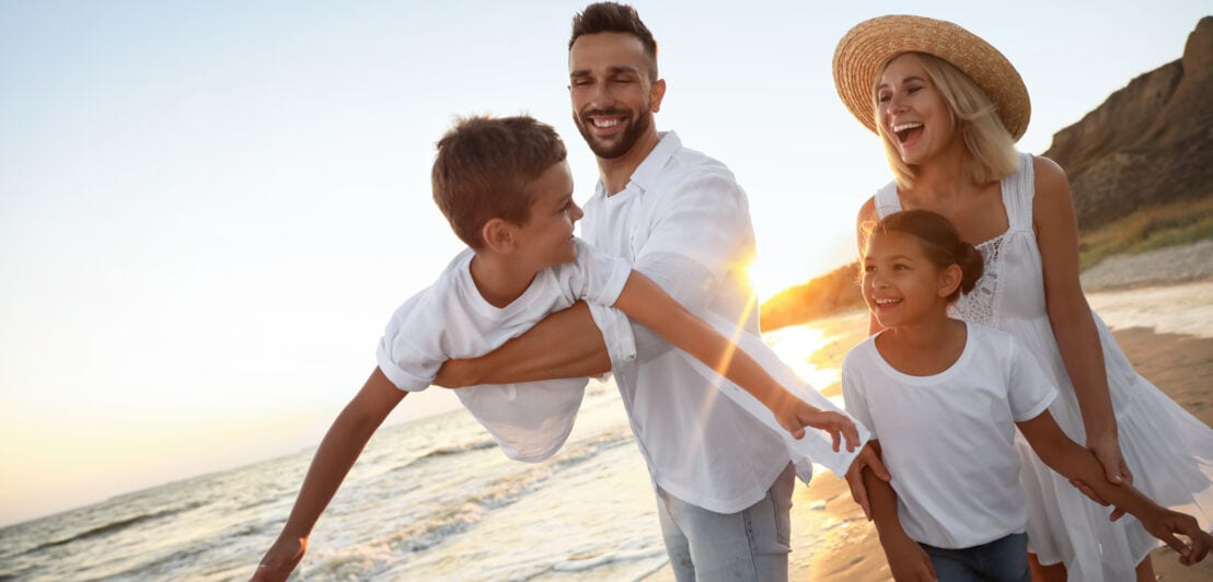 Eine hell gekleidete, glückliche Familie mit zwei Kindern am Strand bei Sonnenuntergang.