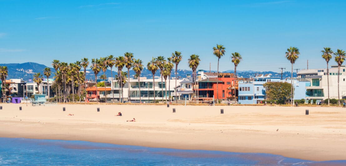 Häuserzeile in Venice Beach, Los Angeles, mit Palmen und Strand, an einem sonnigen Tag.