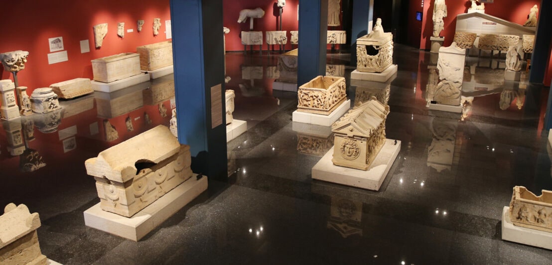 Ein abgedunkelter Ausstellungsraum eines Museums mit zahlreichen Artefakten und Statuen.