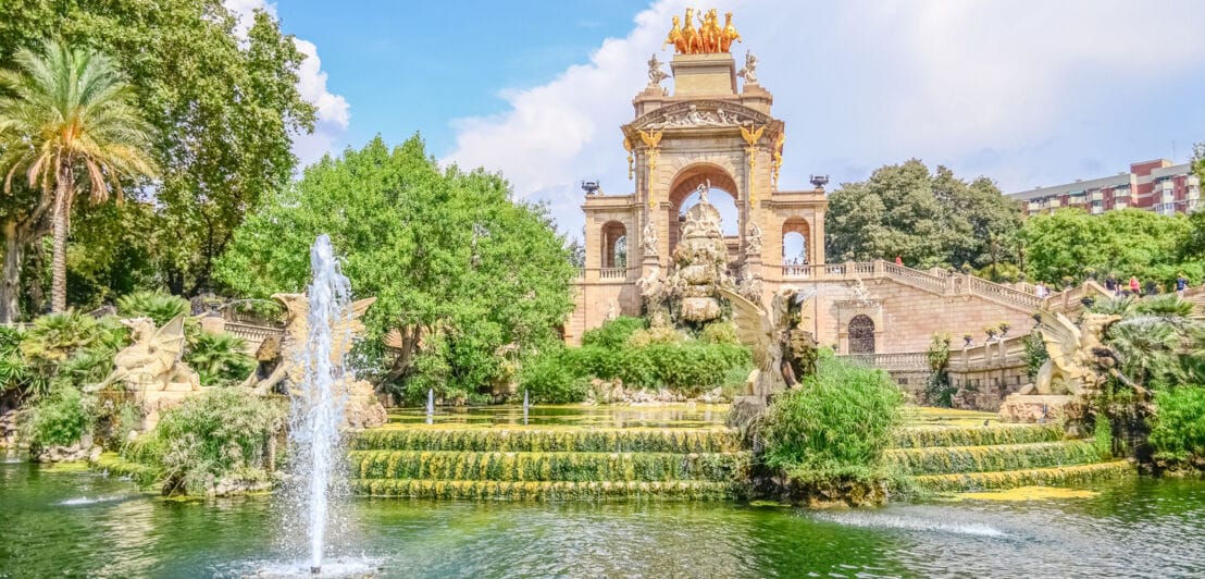 Monumentaler Springbrunnen mit Quadriga in einer üppig begrünten Parkanlage.