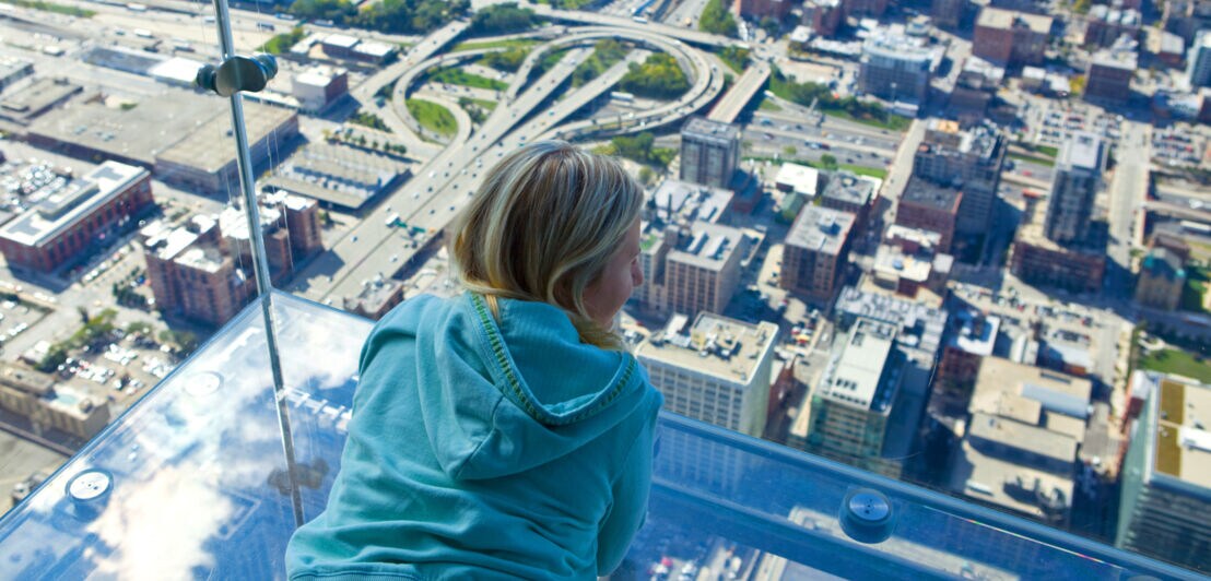 Aufsicht einer auf einem Glasbalkon liegenden Frau über der Skyline Chicagos aus der Vogelperspektive.