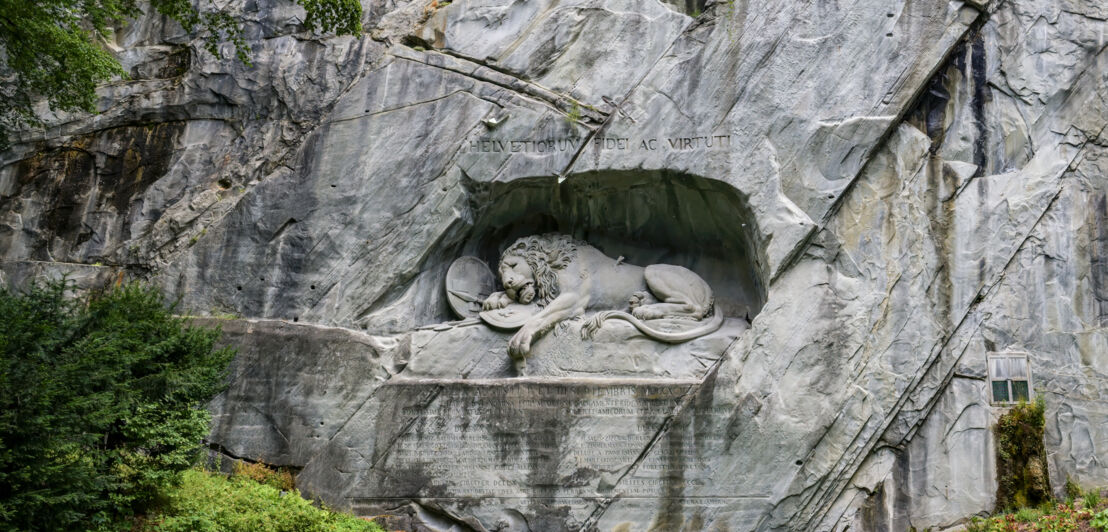Steinskulptur in Löwenform in einer Felswand über einem Teich.