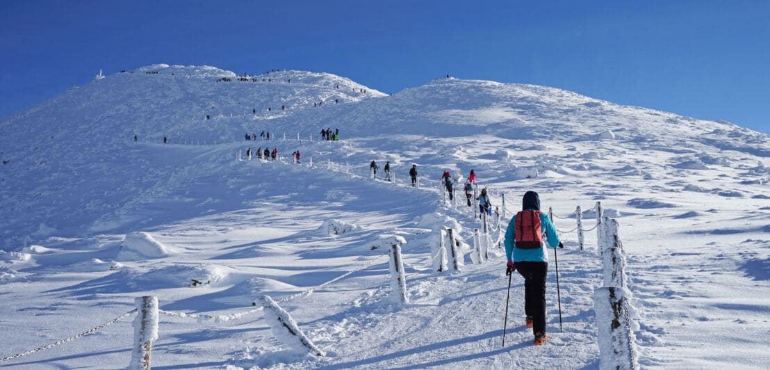 Personen wandern auf einem Weg einen schneebedeckten Hügel hinauf.