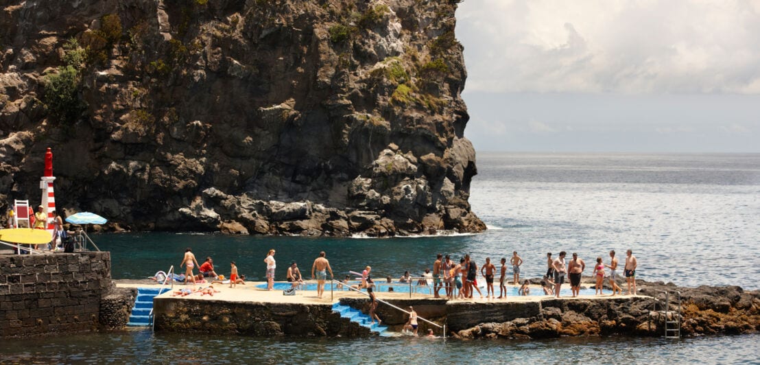 Personen an einem Naturpool in einer Bucht vor Felskulisse.