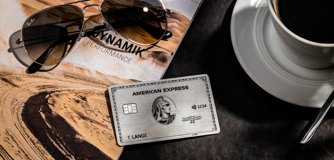 Eine Platinum Card von American Express liegt neben einer Kaffeetasse und einer Sonnenbrille.