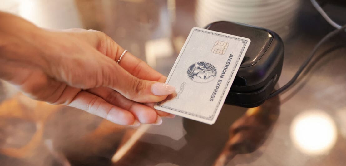 Kartenzahlung mit einer Platinum Card von American Express an einem schwarzen Kartenlesegerät.
