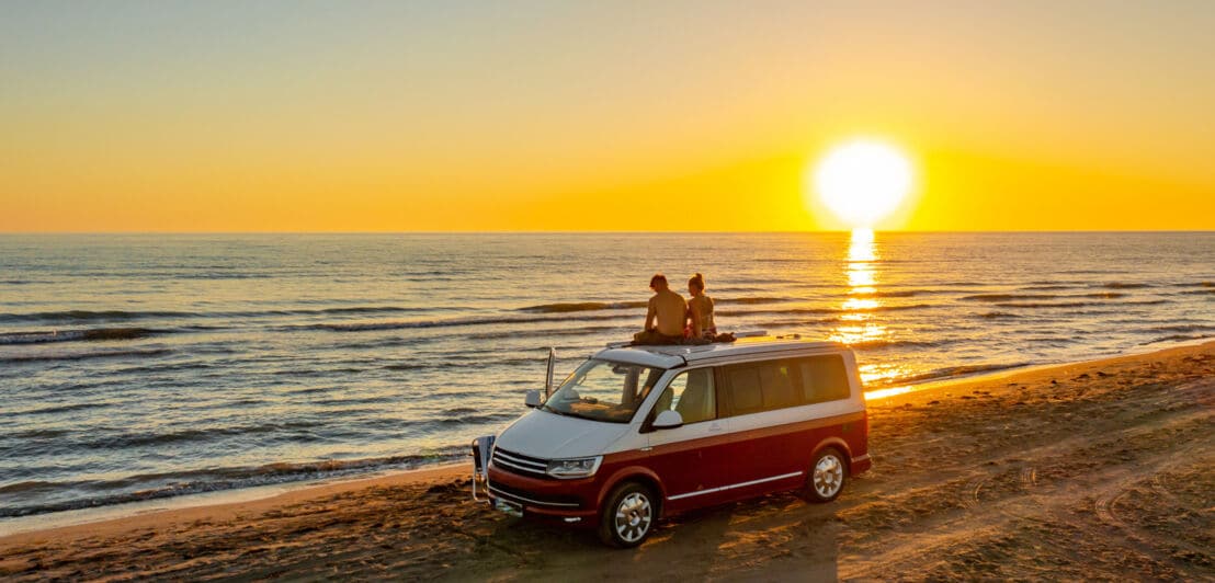 Rückansicht eines Paares auf dem Dach eines Vans am Strand bei Sonnenuntergang.