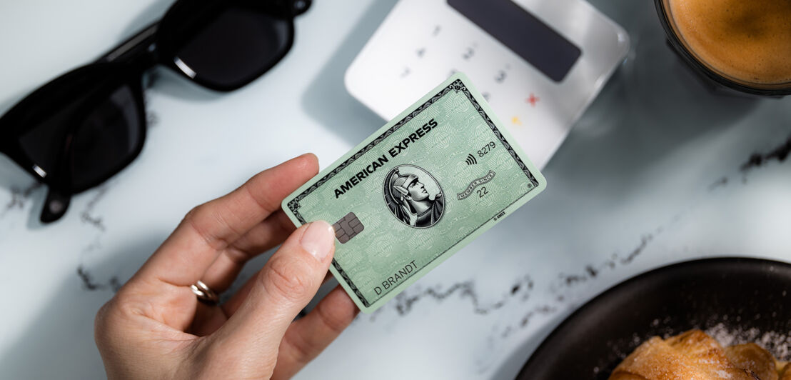 Kontaktlose Zahlung an einem Kartenlesegerät in einem Café mit einer grünen American Express Card