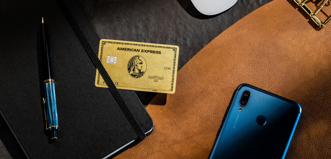 Eine goldene Kreditkarte von American Express liegt auf einem schwarzen Notizblock auf einem Schreibtisch mit edlen Büromaterialien