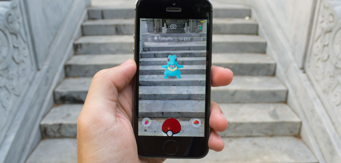 Ein in der Hand gehaltenes Smartphone mit einem blauen Monster in der Pokémon Go AR-App auf dem Display.