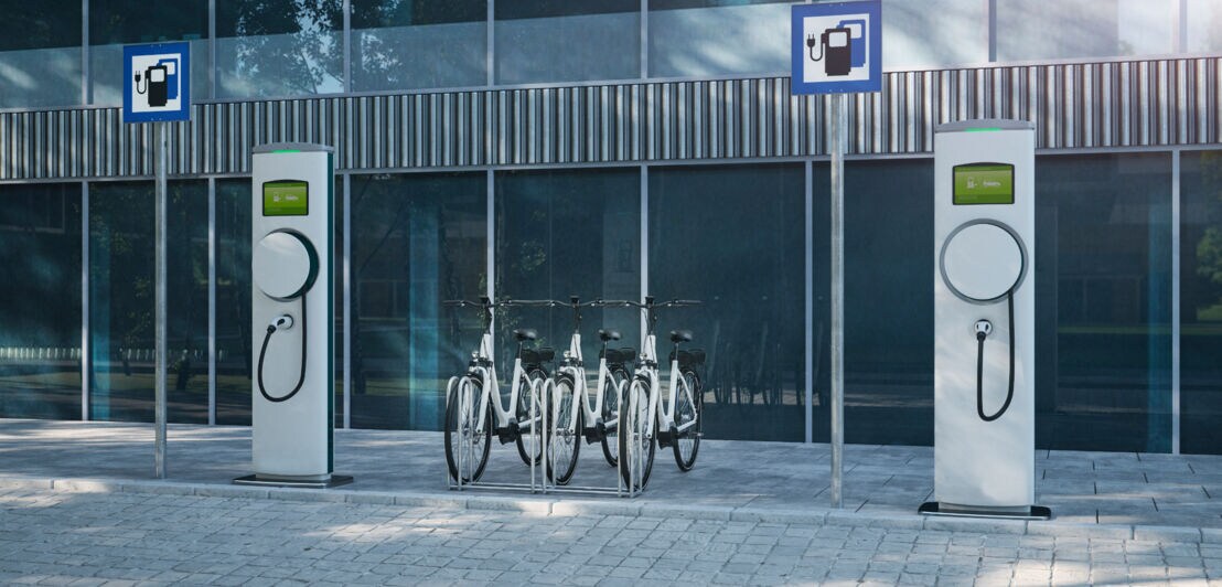 Eine Ladestation für E-Bikes vor einem Bürogebäude mit Glasfassade.