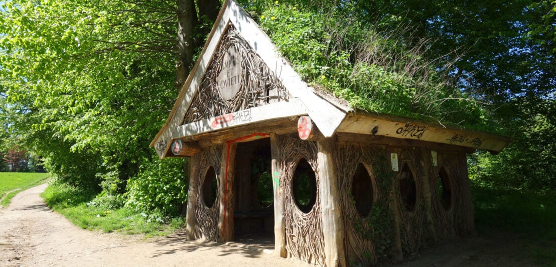 Eine Holzhütte mit einem grasbewachsenen Dach und ovalen Fenstern in einem Park.