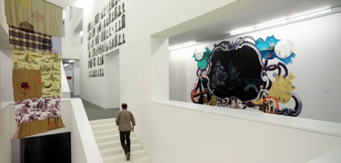 Eine Person läuft in einem Museum mit moderner Kunst eine weiße Treppe hinauf.