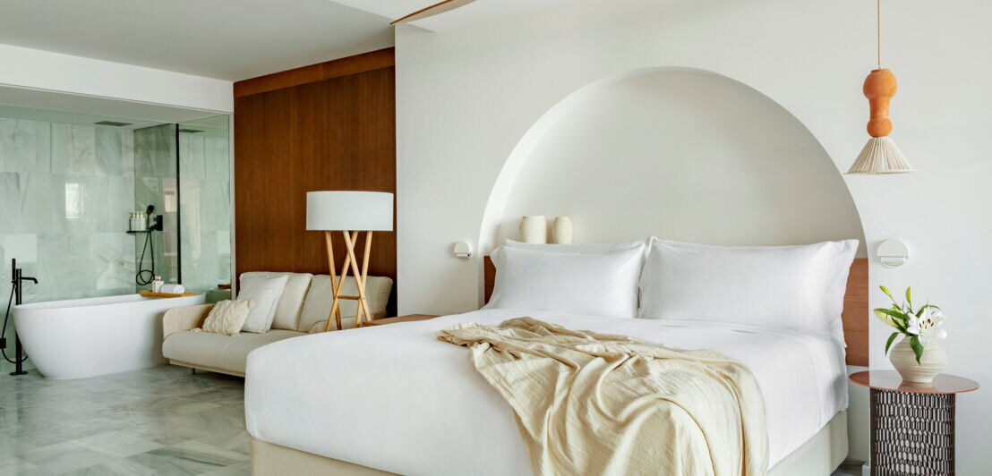 Eine moderne Hotelsuite in hellen Tönen mit Doppelbett und Badewanne.