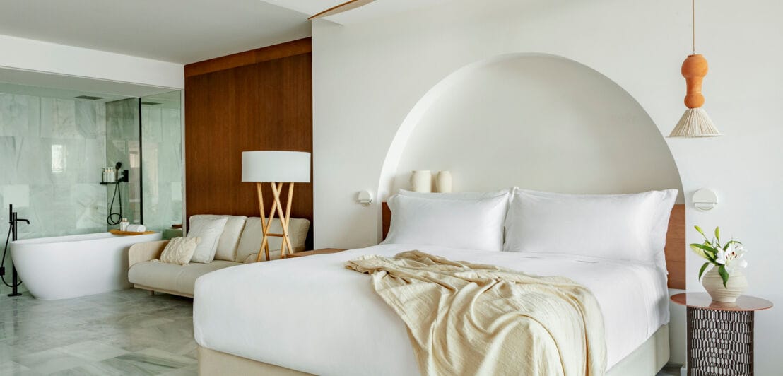 Eine moderne Hotelsuite in hellen Tönen mit Doppelbett und Badewanne.