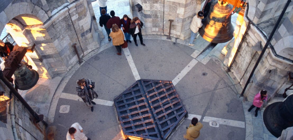 Aufsichtaufnahme von Personen auf einer Aussichtsplattform eines runden Turms mit Glocken.