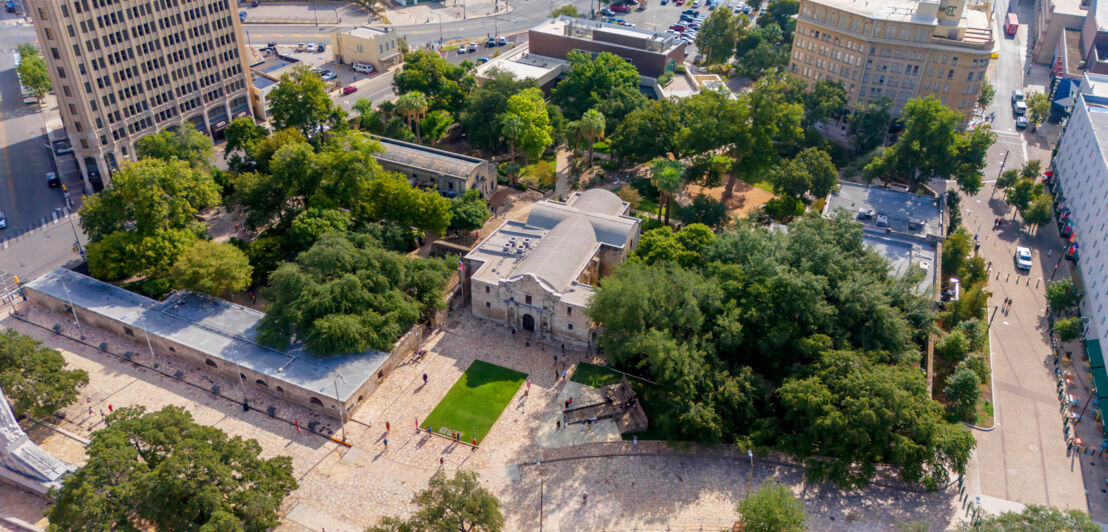 Gebäudekomplex der Missionsstätte The Alamo mit Kirche und Garten im Stadtzentrum aus der Luftperspektive.