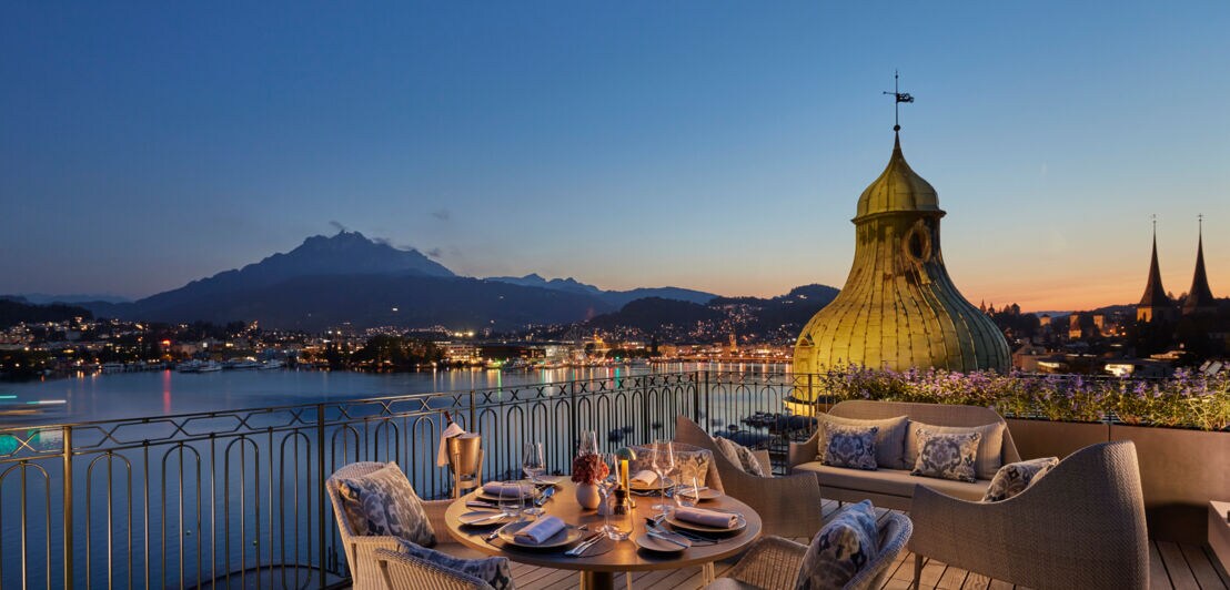 Elegante Hotelterrasse am See mit Blick auf Luzern in der Abenddämmerung.