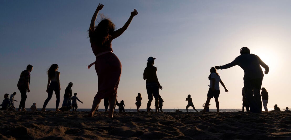Silhouetten mehrerer tanzender Personen am Strand.