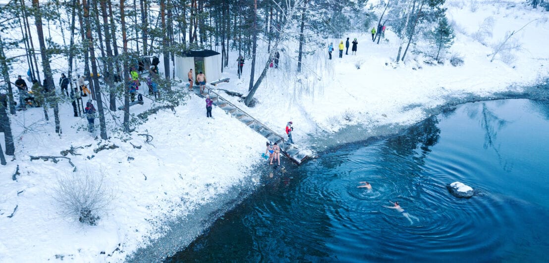 Luftaufnahme von Menschen, die in einem von Schnee umgebenen See baden.