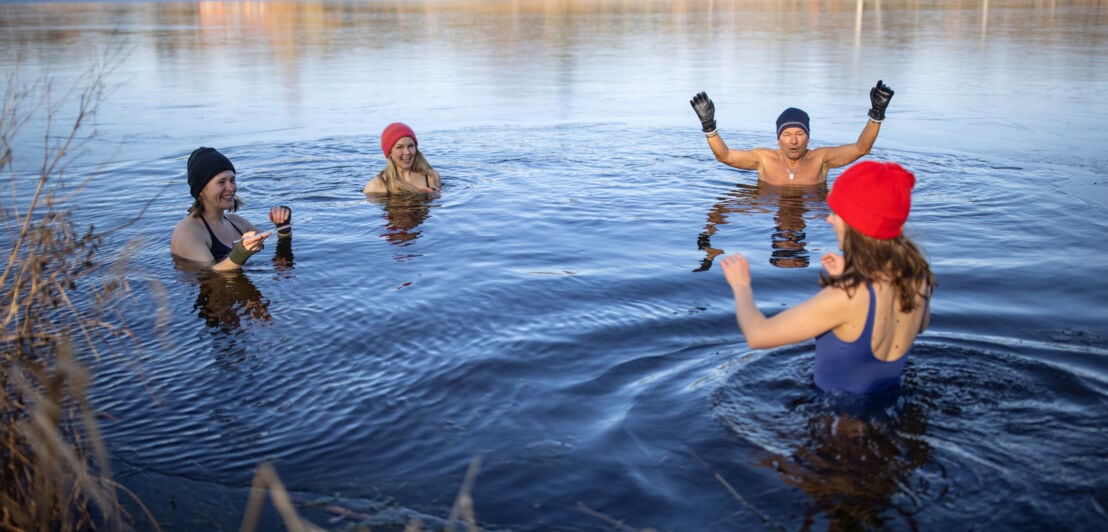 Vier Personen mit Mützen baden in einem See im Winter.