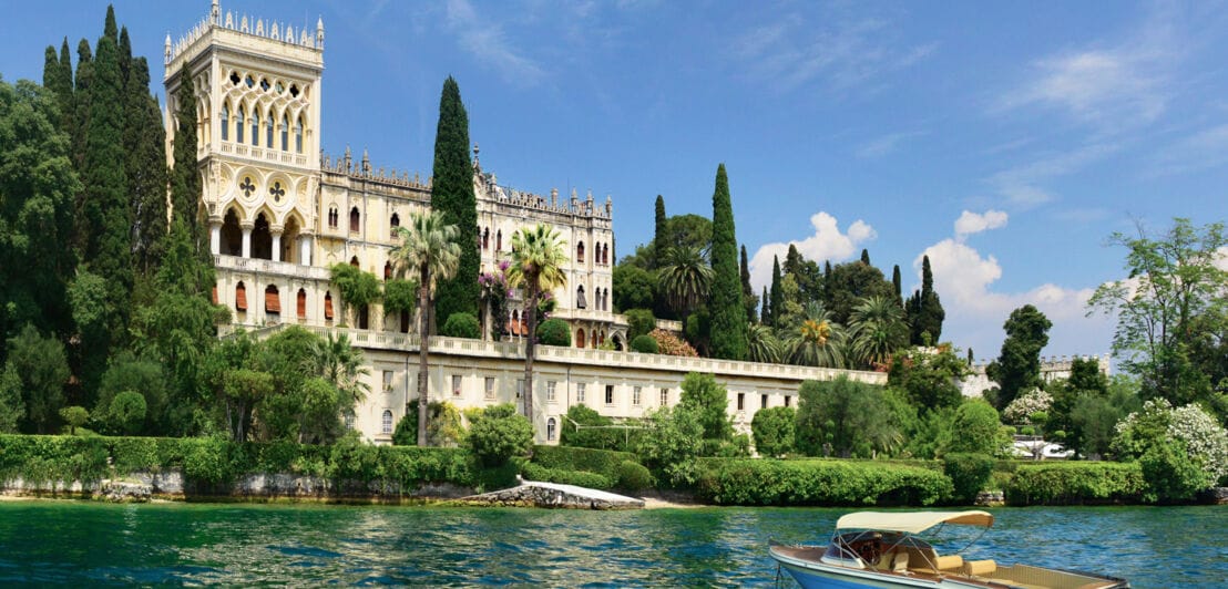 Eine pittoreske Villa im venezianischen Stil, umgeben von einer Parkanlage, am Ufer eines Sees mit Boot.