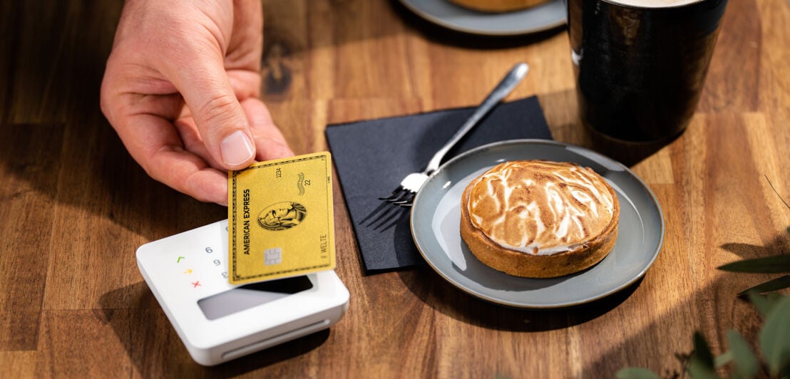 Kontaktlose Zahlung an einem Kartenlesegerät mit einer American Express Gold Card in einem Café.
